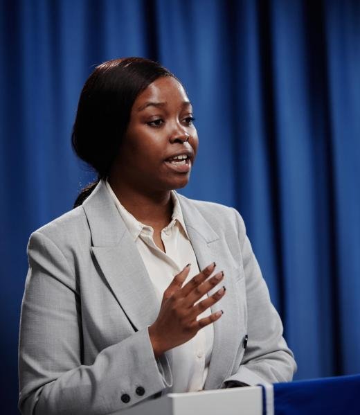 Young confident African American female delegate in formalwear speaking to public or press while standing by platform at political forum
